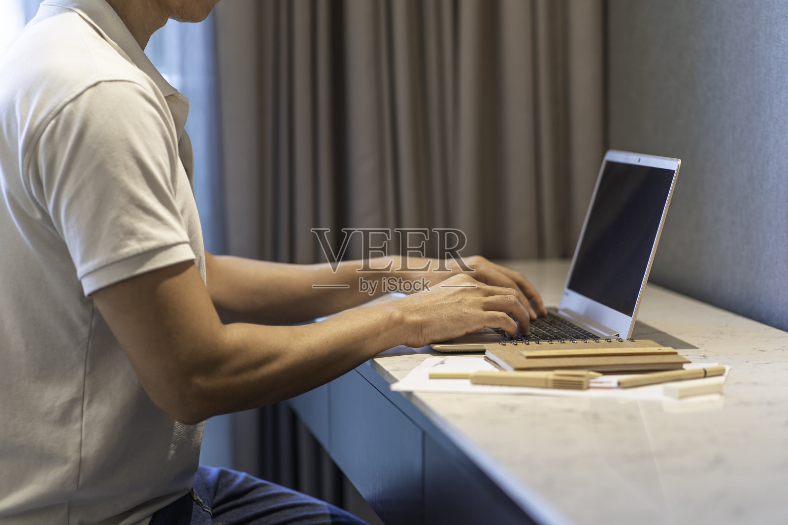 亚洲人穿着休闲的白色polo衫和牛仔裤在桌上使用笔记本电脑照片摄影图片