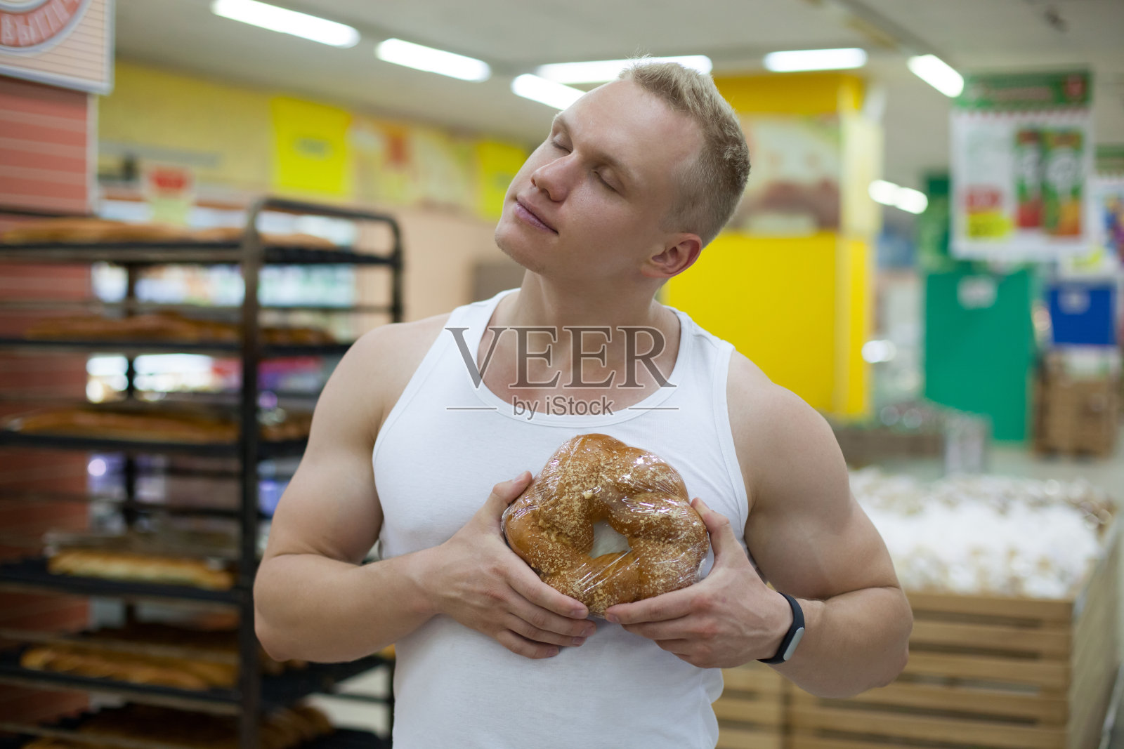 肌肉发达的男运动员闭着眼睛抱着一条面包梦游地站在杂货店里照片摄影图片