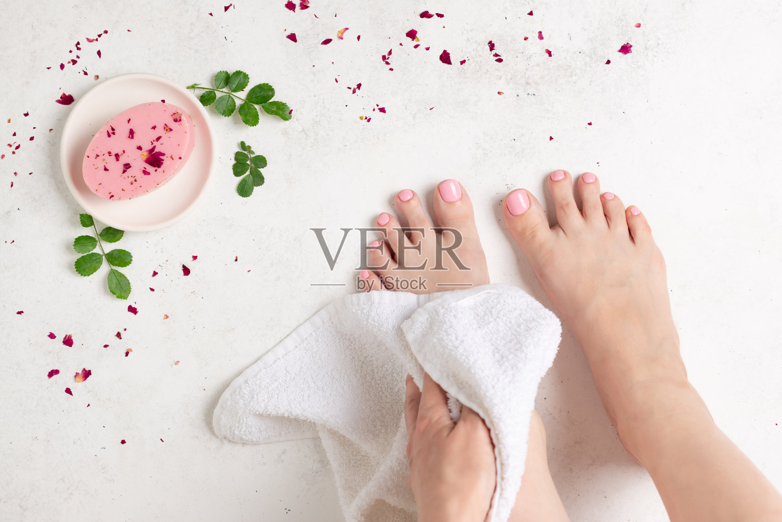 年轻女子照顾她的腿与一个美丽的粉红色足疗。天然玫瑰皂，花瓣和绿叶照片摄影图片