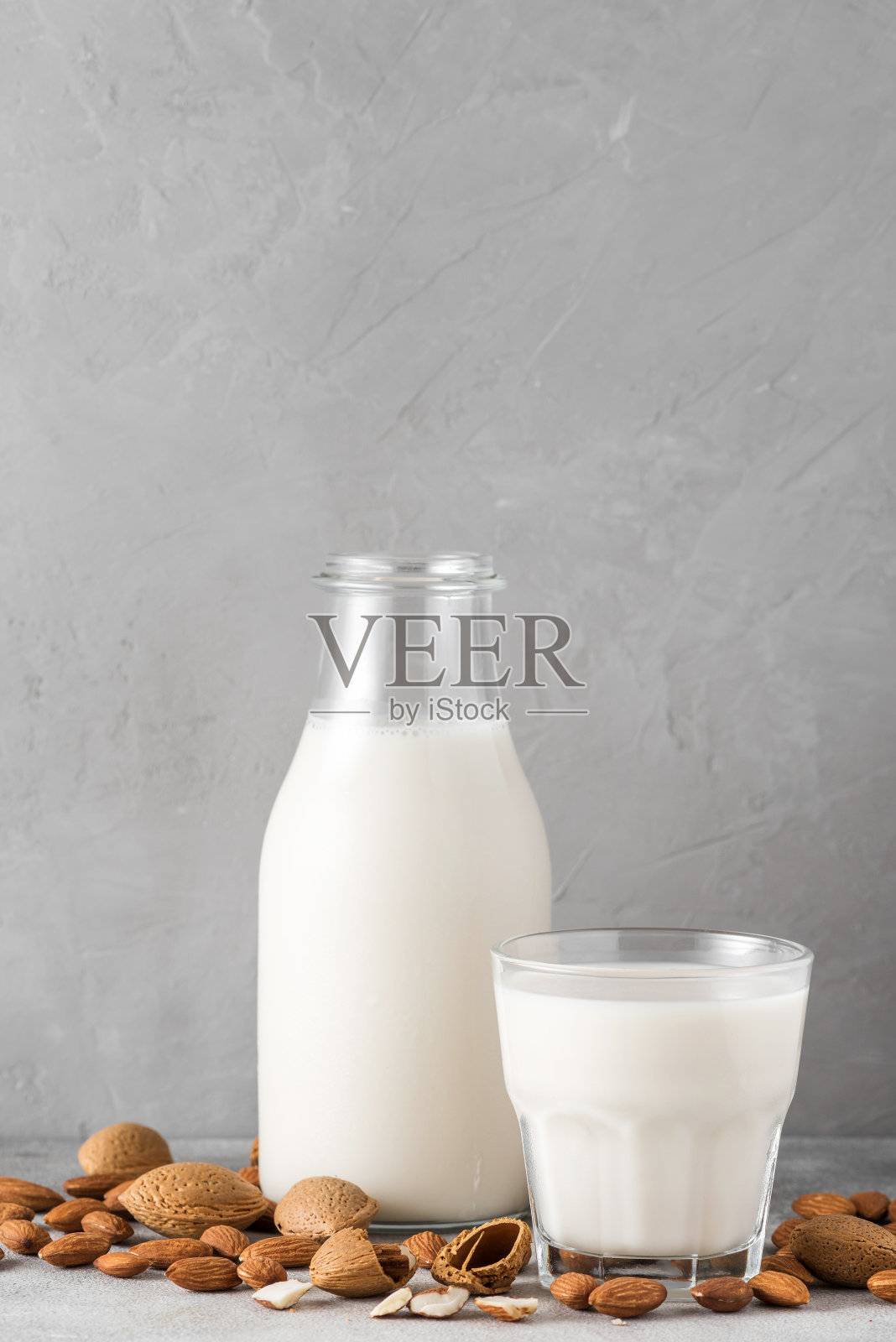 杏仁牛奶在一个瓶子与玻璃和杏仁坚果在混凝土背景。不含植物奶的素食乳制品。垂直方向照片摄影图片