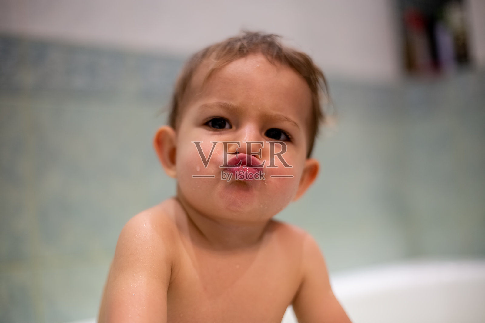 一个正在洗澡的可爱宝宝看着镜头亲吻。软对焦，特写，背景-模糊的家庭浴室照片摄影图片