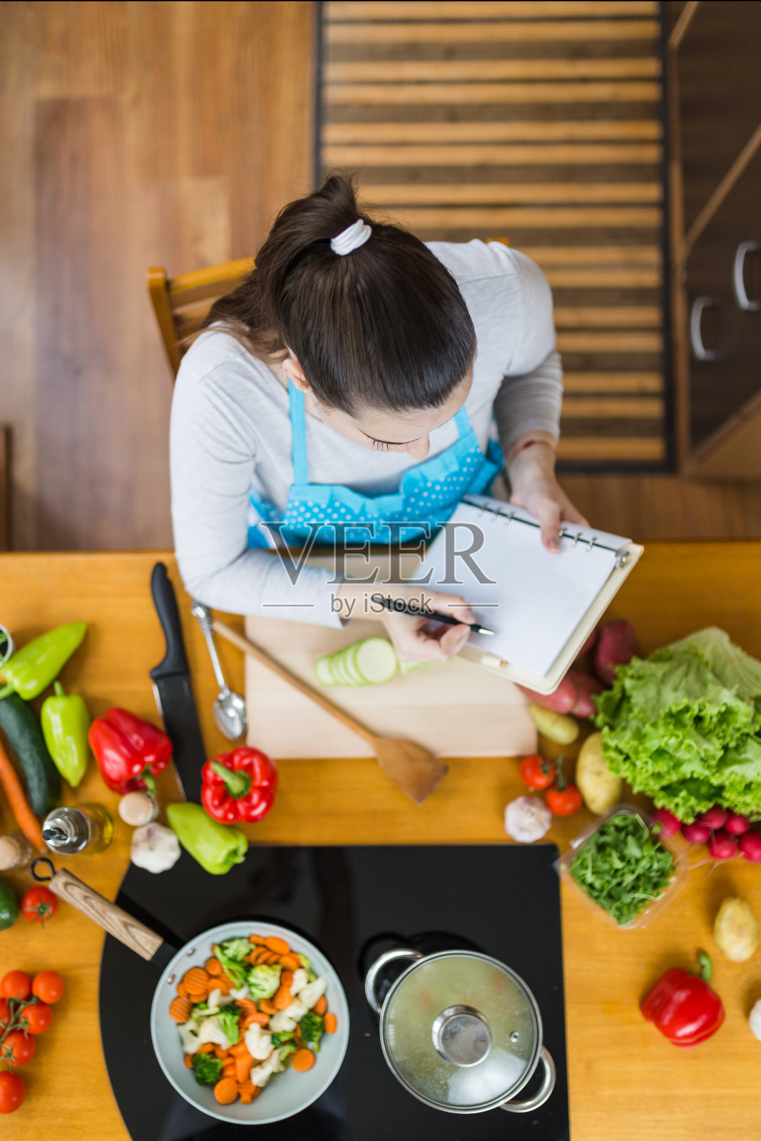 以上观点的家庭主妇坐在厨房桌子上阅读或记录健康的烹饪食谱。照片摄影图片