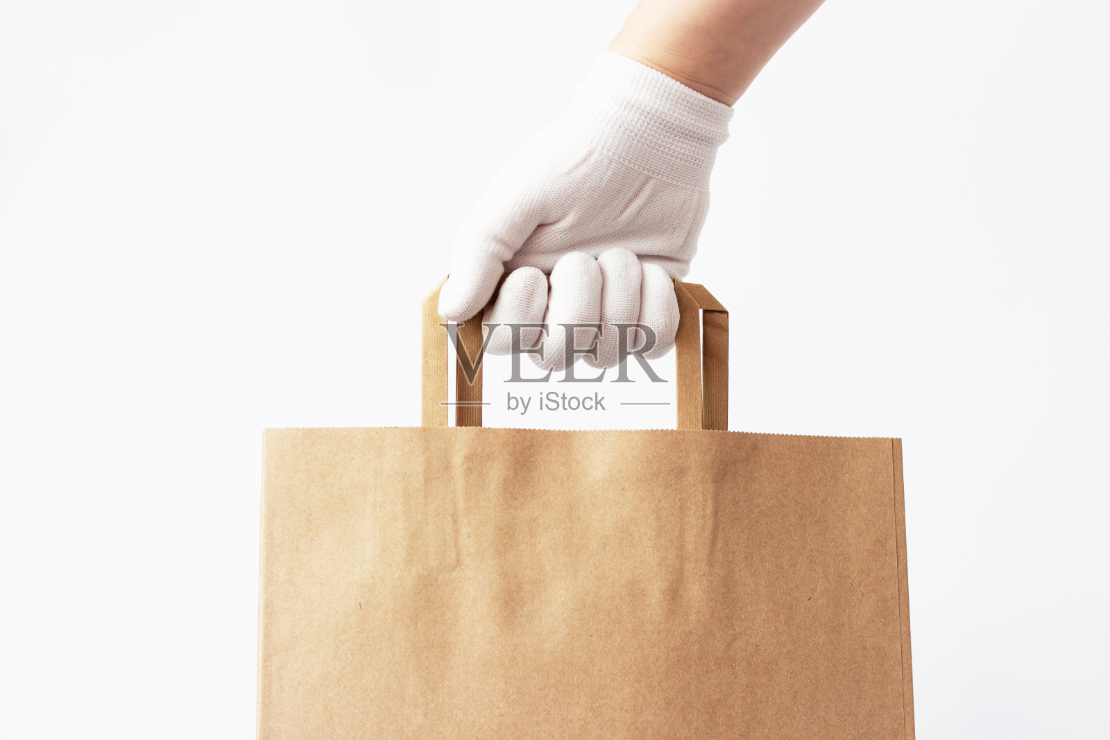 女性的手在一个手套持有棕色的硬纸板袋在白色的背景，食品配送的概念。照片摄影图片