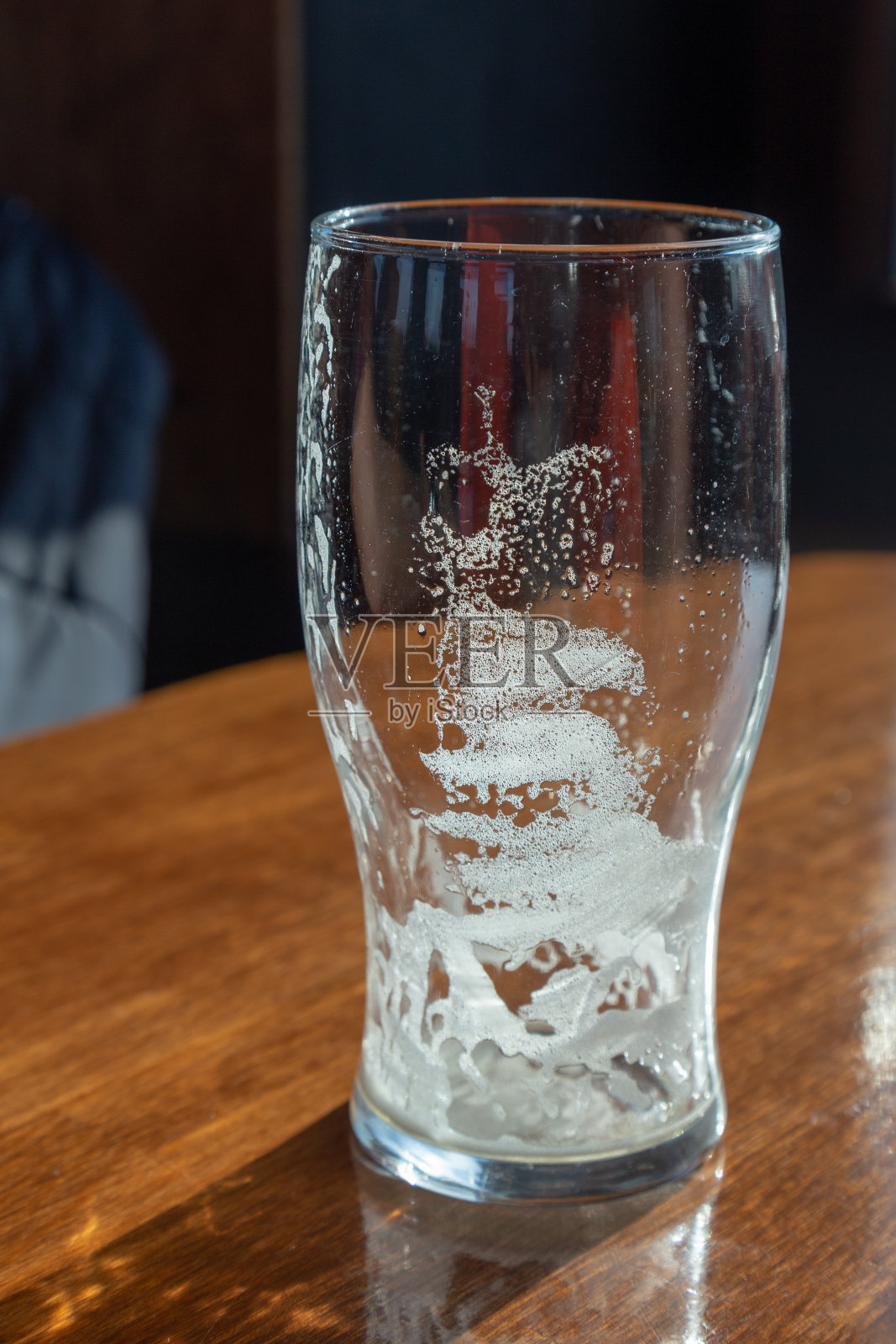 酒吧的桌子上放着一只空啤酒杯，被窗外的阳光照得亮晶晶的。照片摄影图片