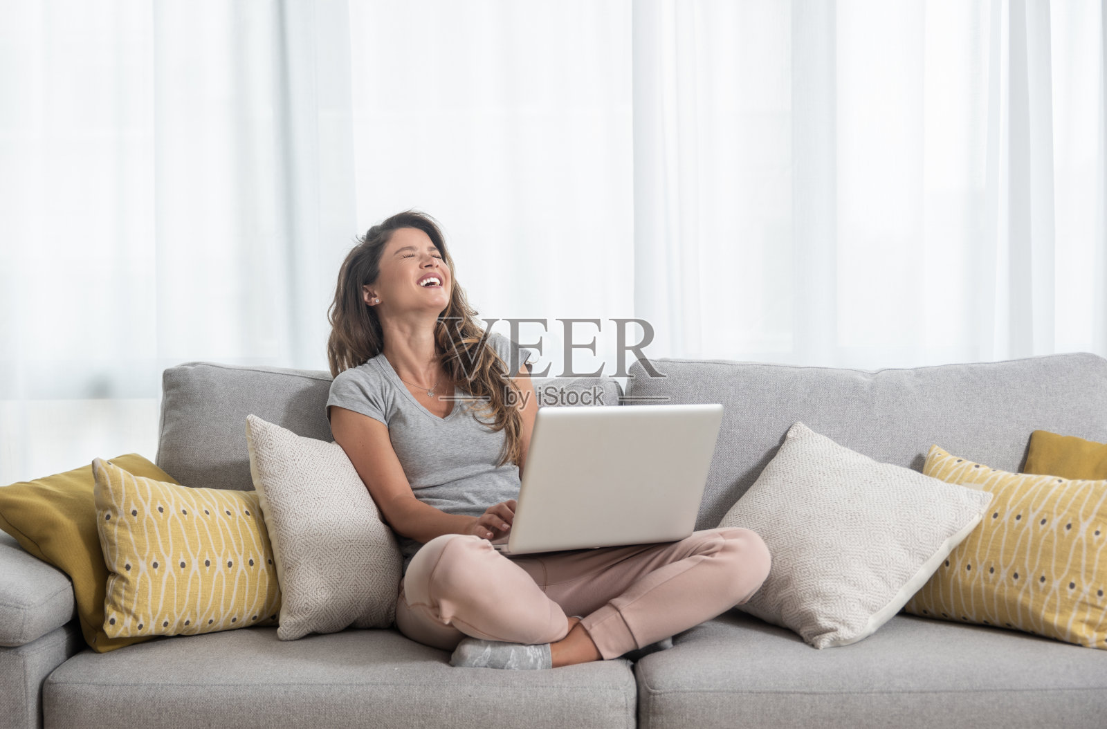 年轻漂亮的单身女人和她的男朋友或女朋友聊天坐在沙发上的笔记本电脑和大笑照片摄影图片