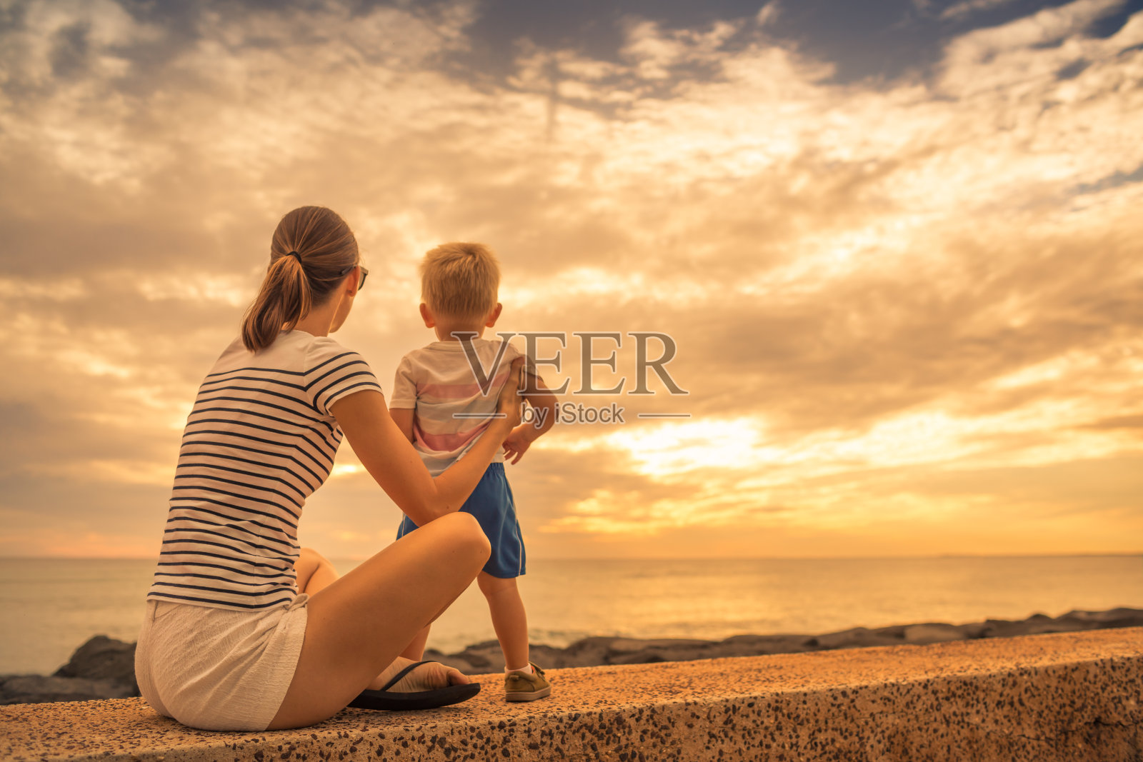 母亲和儿子在欣赏美丽的日落。照片摄影图片