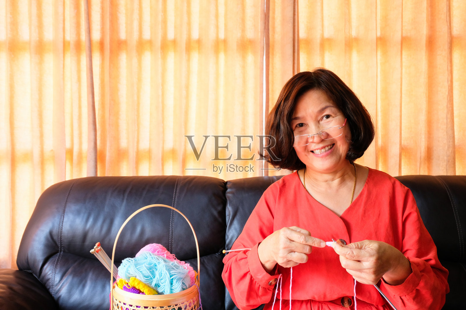 年长的亚洲妇女坐在沙发沙发上微笑着编织五彩缤纷的纱线。快乐轻松的退休生活方式。与复制空间的文本。照片摄影图片