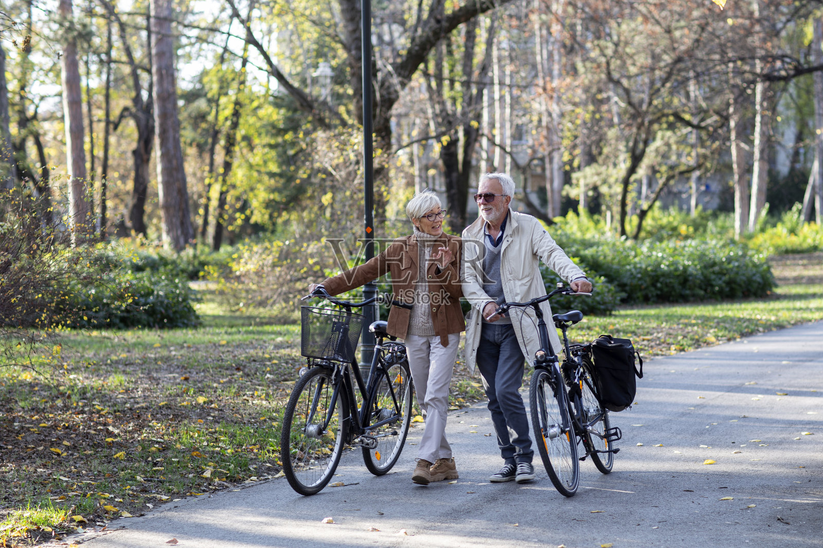 一对成熟的情侣在公园里推着自行车谈笑风生照片摄影图片