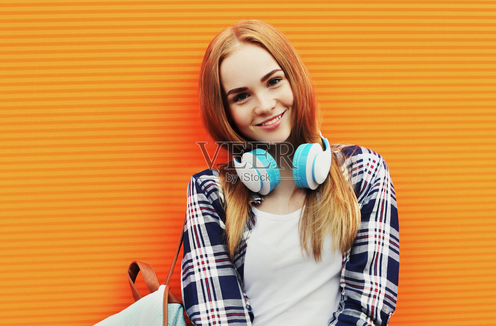 快乐的微笑女人的肖像在无线耳机听音乐在多彩的橙色背景照片摄影图片