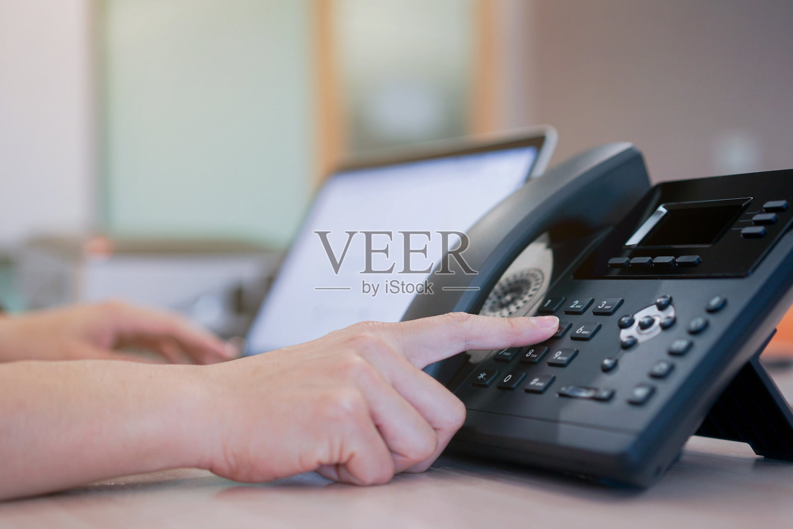 近距离的员工手工按下VOIP电话上的按键号码，与合作伙伴或同事在操作室的办公桌旁进行沟通，技术电信的概念照片摄影图片
