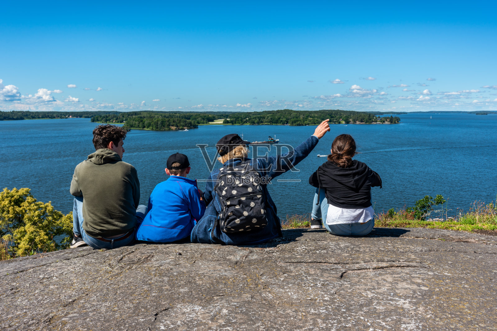 一家人坐在山顶上俯瞰着湖Mälaren的水对着地平线。照片摄影图片