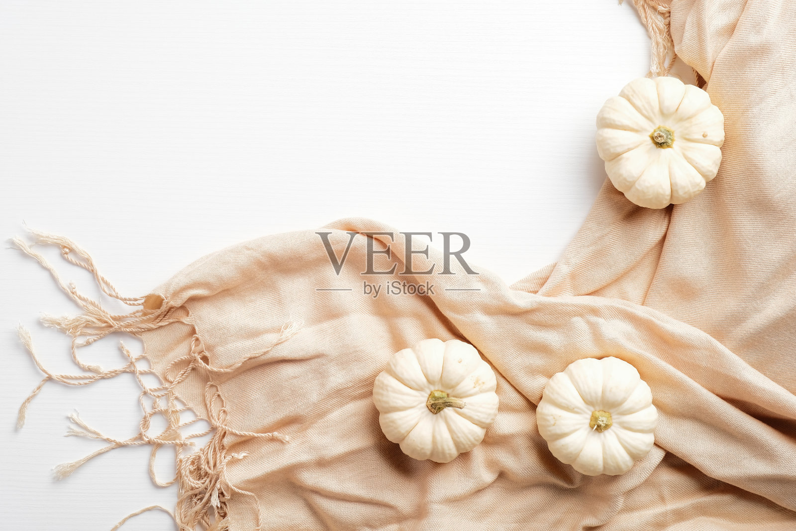 优雅的秋天组成。白色的小南瓜和米色的围巾放在白色的桌子上。秋天的时尚概念。照片摄影图片