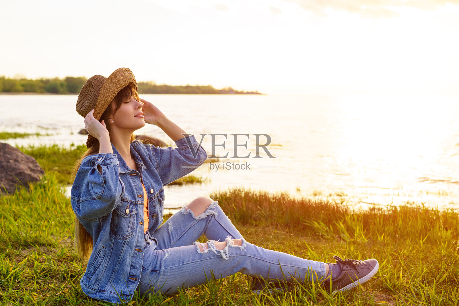 戴着帽子和牛仔裤的女人坐在大海的背景上照片摄影图片
