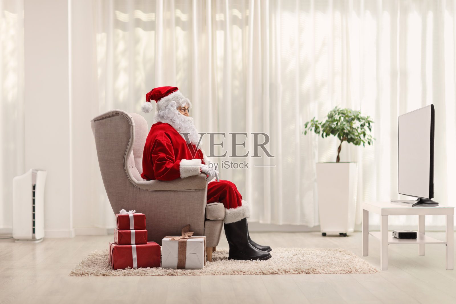 圣诞老人坐在扶手椅上看电视照片摄影图片