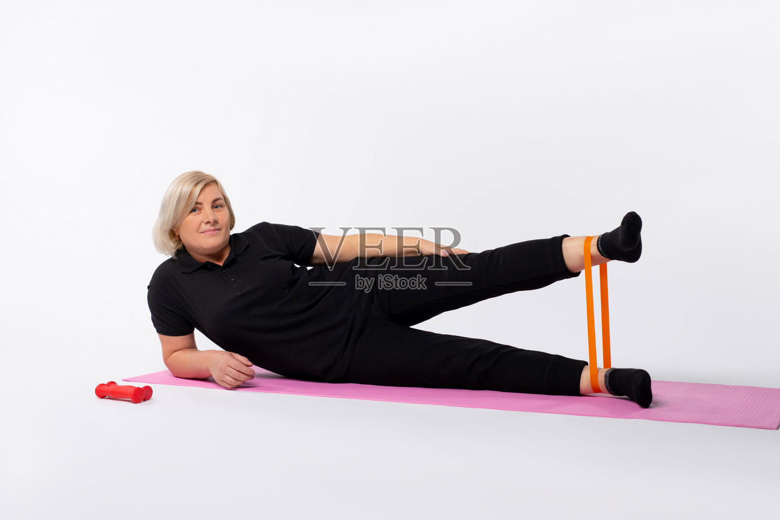 运动的老年妇女在家里做健身运动的阻力橡皮筋躺在垫子上。健康的生活方式概念。照片摄影图片
