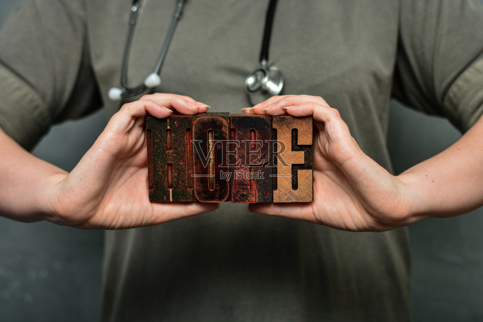 一名医务工作者手持听诊器，举着由木制印刷字体制成的“希望”字照片摄影图片