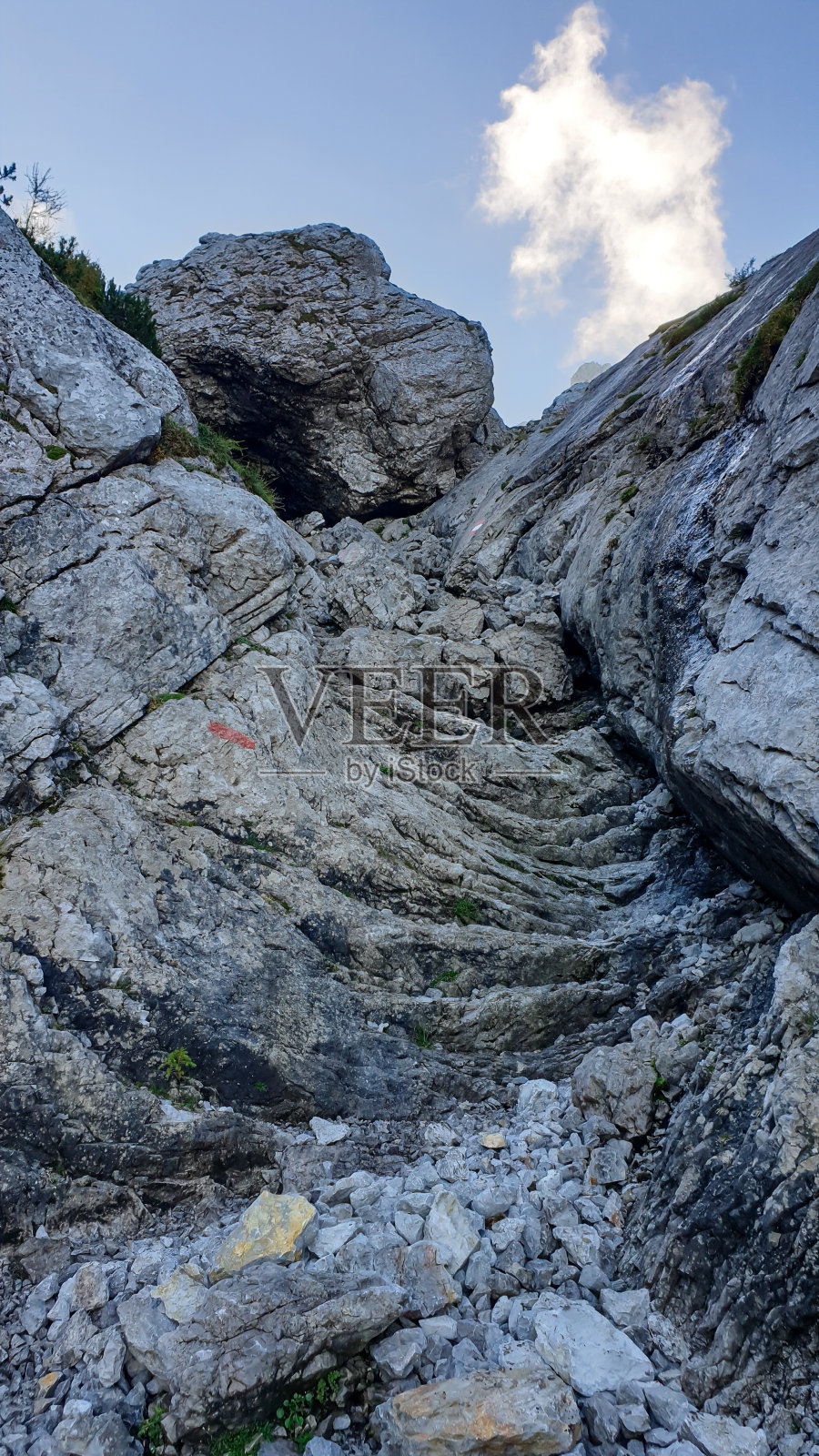 在前往奥地利阿尔卑斯山格林明的路上，陡峭的山壁。只有专业人士才有危险的攀登。它上面的天空是蓝色的，一小朵云。极限运动。旁边有红色的路径标记。照片摄影图片