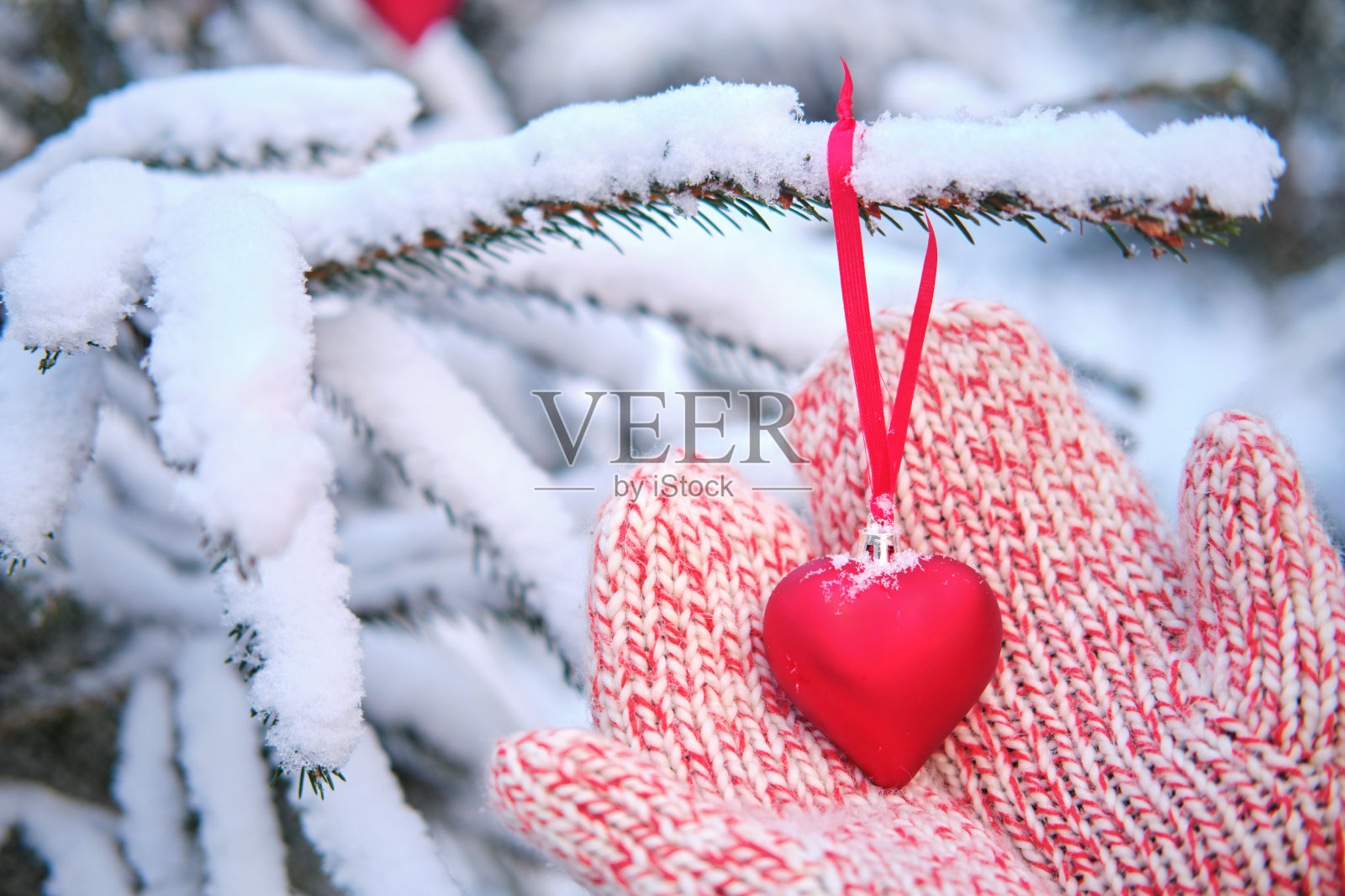 小女孩双手握着一个心形的圣诞树玩具。在白雪覆盖的公园里过新年照片摄影图片