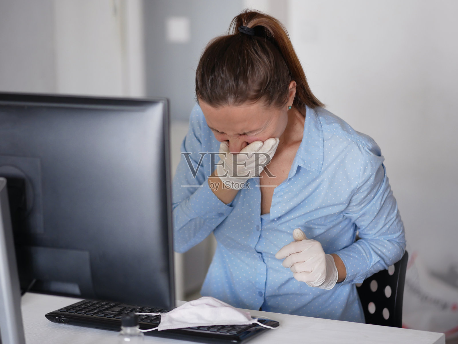 生病的年轻女子戴着口罩使用笔记本电脑并咳嗽，在家或在办公室工作，关闭照片摄影图片