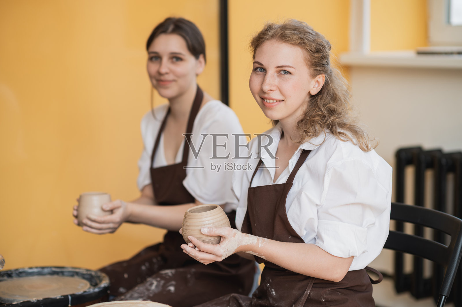 在陶艺坊，两个女孩在陶艺轮上制作陶土手工工艺，友情和指导理念照片摄影图片