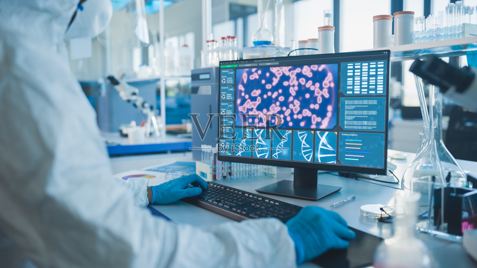 医学实验室:微生物学家穿着无菌工作服，面罩和电脑研制疫苗，药物和抗生素。屏幕显示DNA研究的概念。照片摄影图片