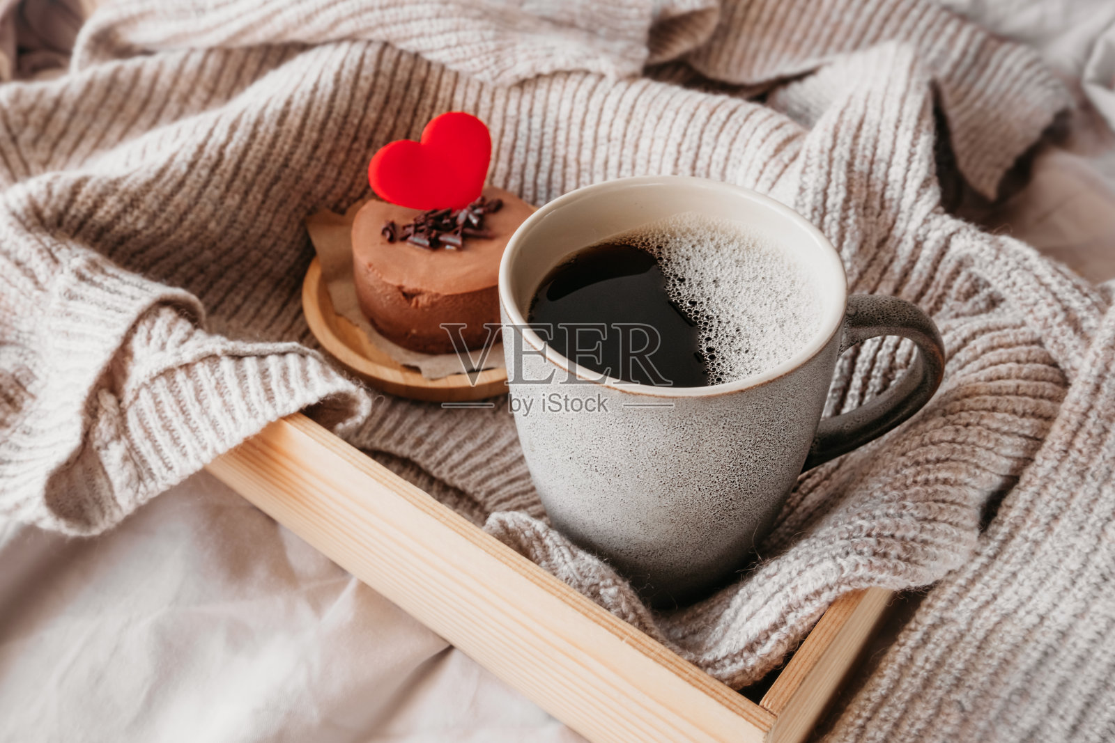 陶瓷灰色杯黑咖啡和圆形巧克力小芝士蛋糕在舒适的气氛下与皱褶的织物。给爱的人惊喜，情人节的礼物创意，选择性的关注照片摄影图片