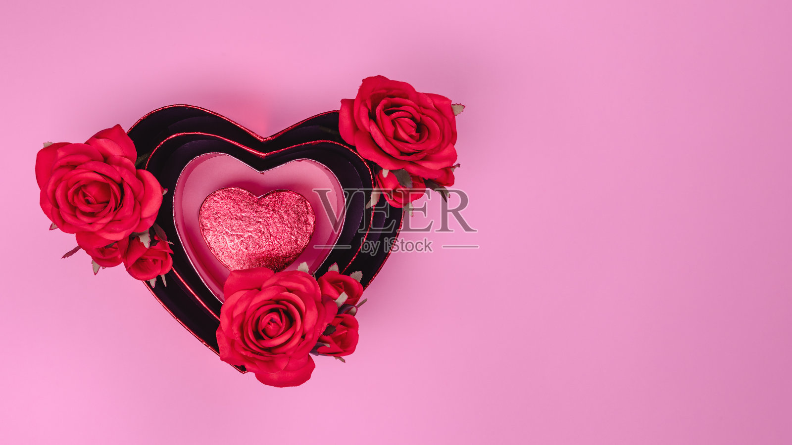 红色美丽的玫瑰在心形礼品盒与红色的心在粉红色的背景。照片摄影图片