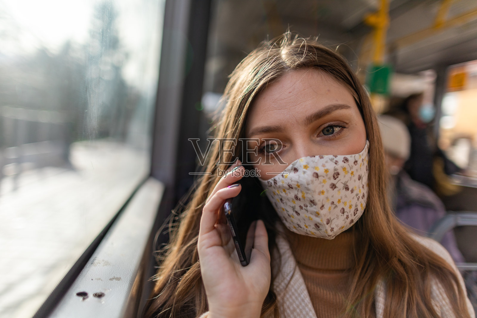 抑郁的女人戴着保护面罩，在乘公共汽车时用手机和看窗户照片摄影图片