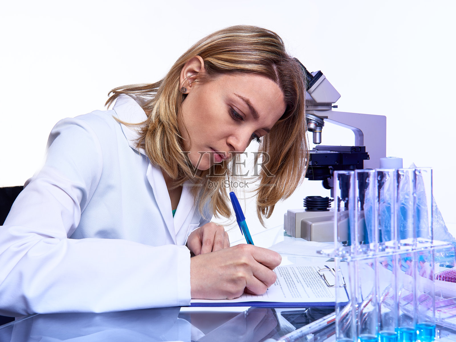 年轻的女性科学家或技术人员在现代实验室用显微镜，玻璃管样品和定时器，霓虹灯色调图像写报告或实验室杂志照片摄影图片