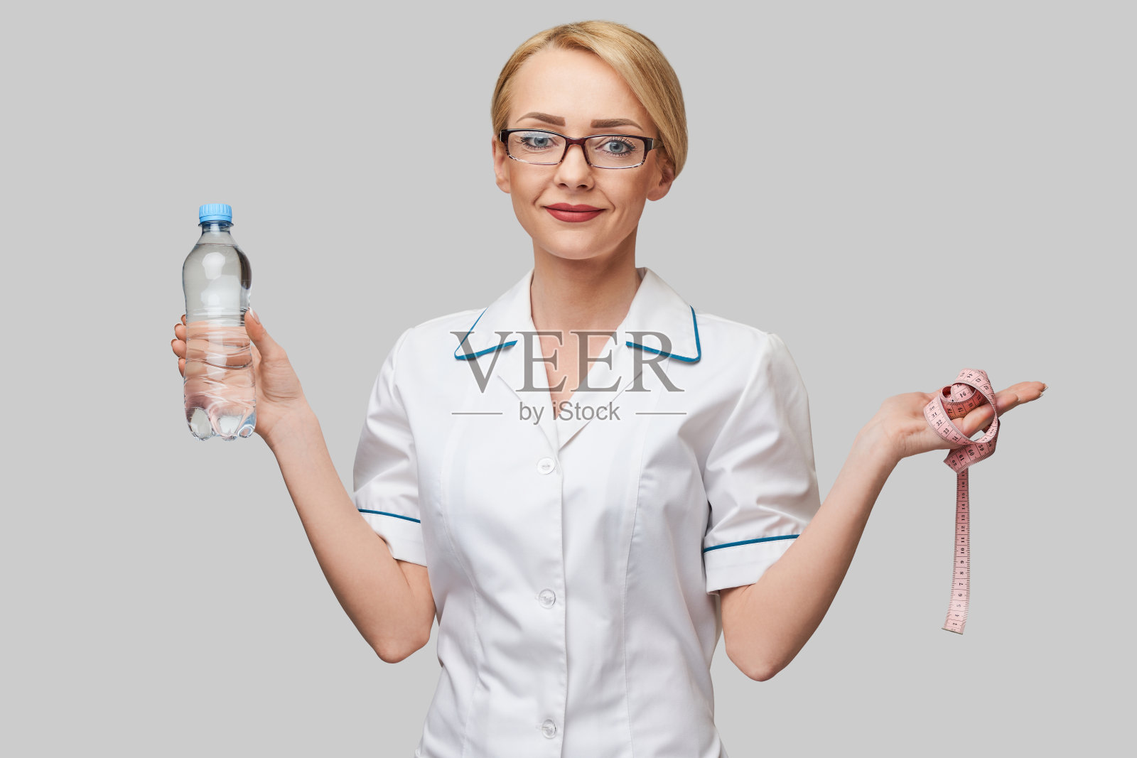 年轻的白种人妇女健康护理专业人员的肖像拿着水和测量带站在浅灰色的背景照片摄影图片
