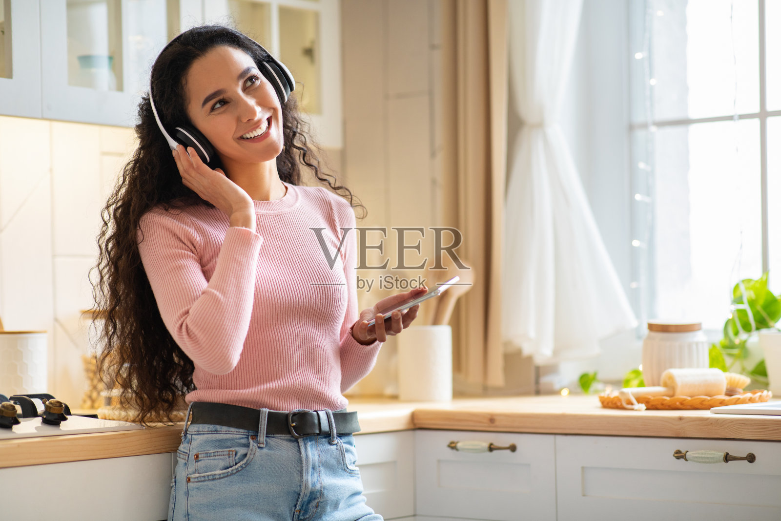 快乐的黑发女人戴着耳机在厨房里用智能手机听音乐照片摄影图片