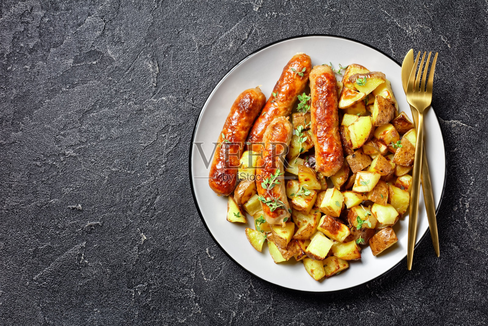 香肠和烤土豆放在盘子里，用金色的刀叉放在水泥桌子上，平铺，空间大照片摄影图片
