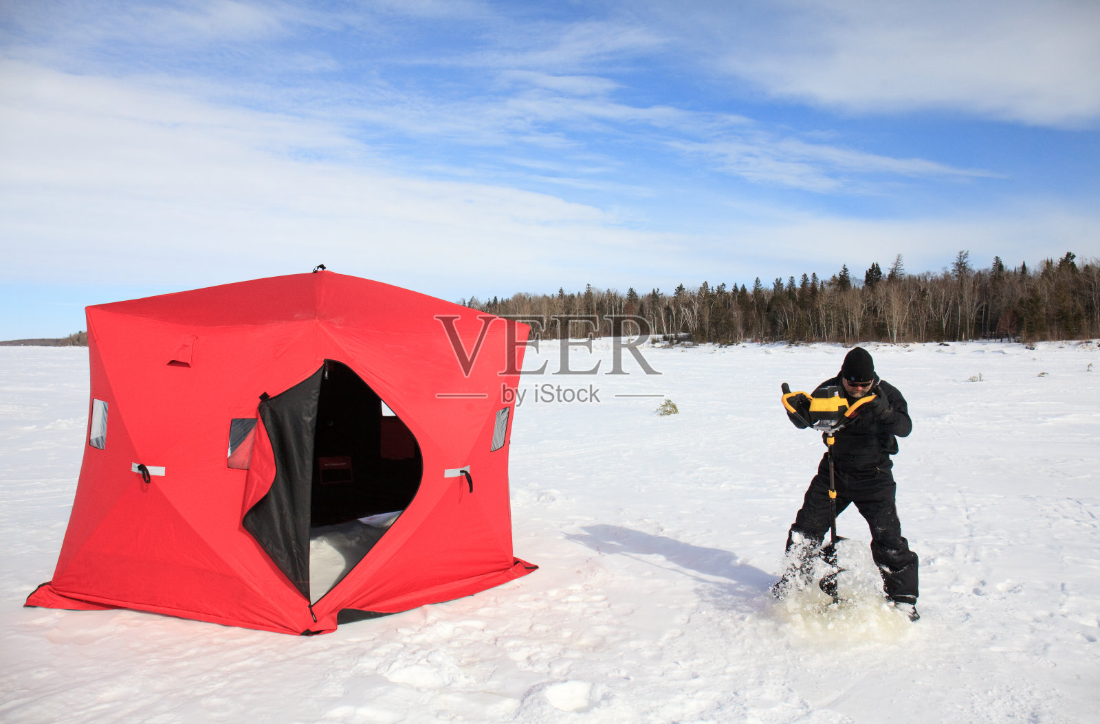 在加拿大马尼托巴省，一名男子用螺旋钻在冰上钻孔，用于冰上捕鱼照片摄影图片
