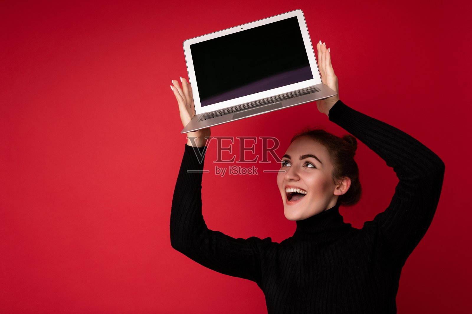 美丽的微笑幸福年轻的黑发女人拿着电脑笔记本电脑空屏幕穿着黑色长袖看着上网本孤立在红色的背景照片摄影图片