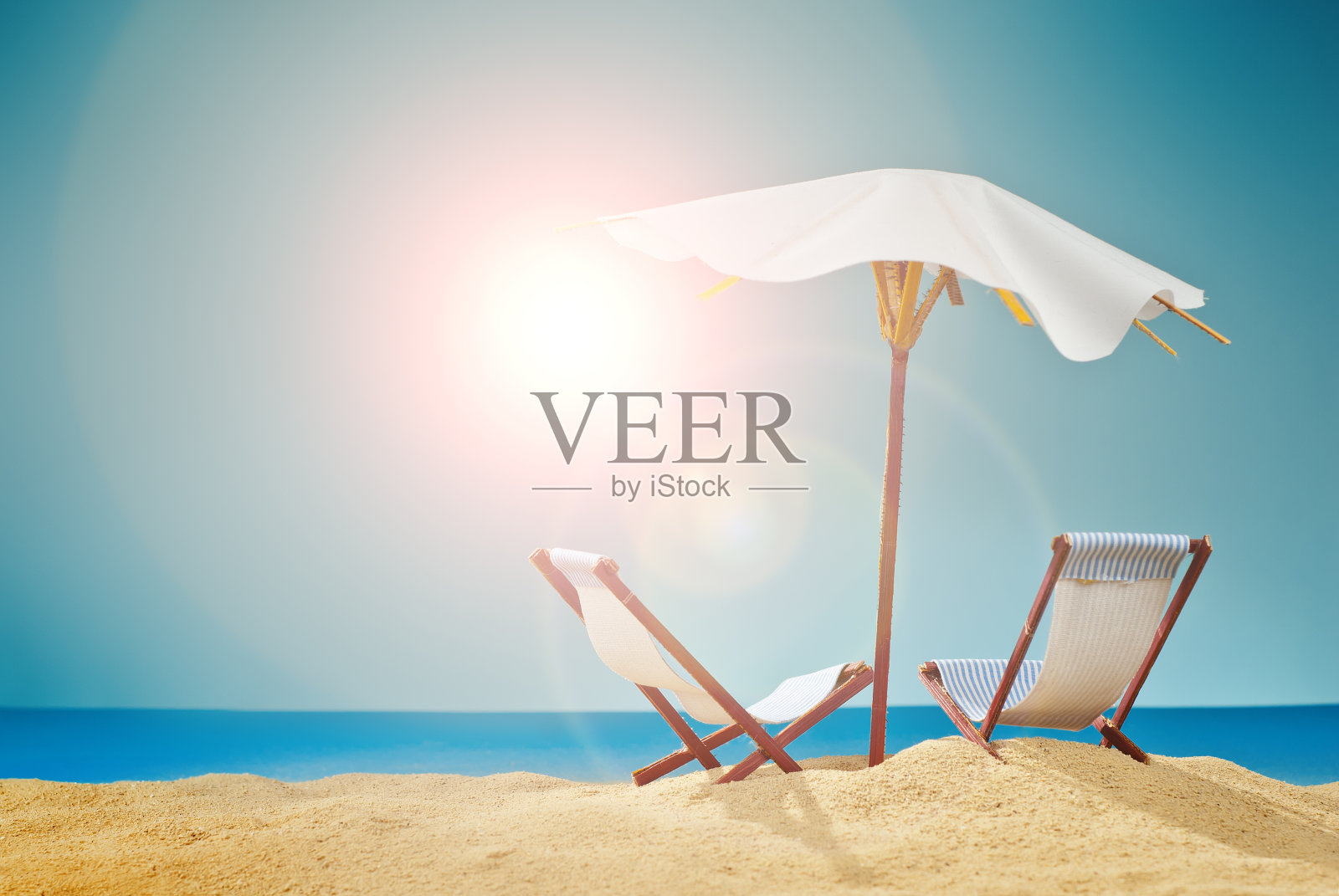 沙滩上有遮阳伞和日光浴床。程式化的纸板海滩。背景是用来喝鸡尾酒的纸伞。休息、海洋和度假的概念。人造木制甲板椅。照片摄影图片