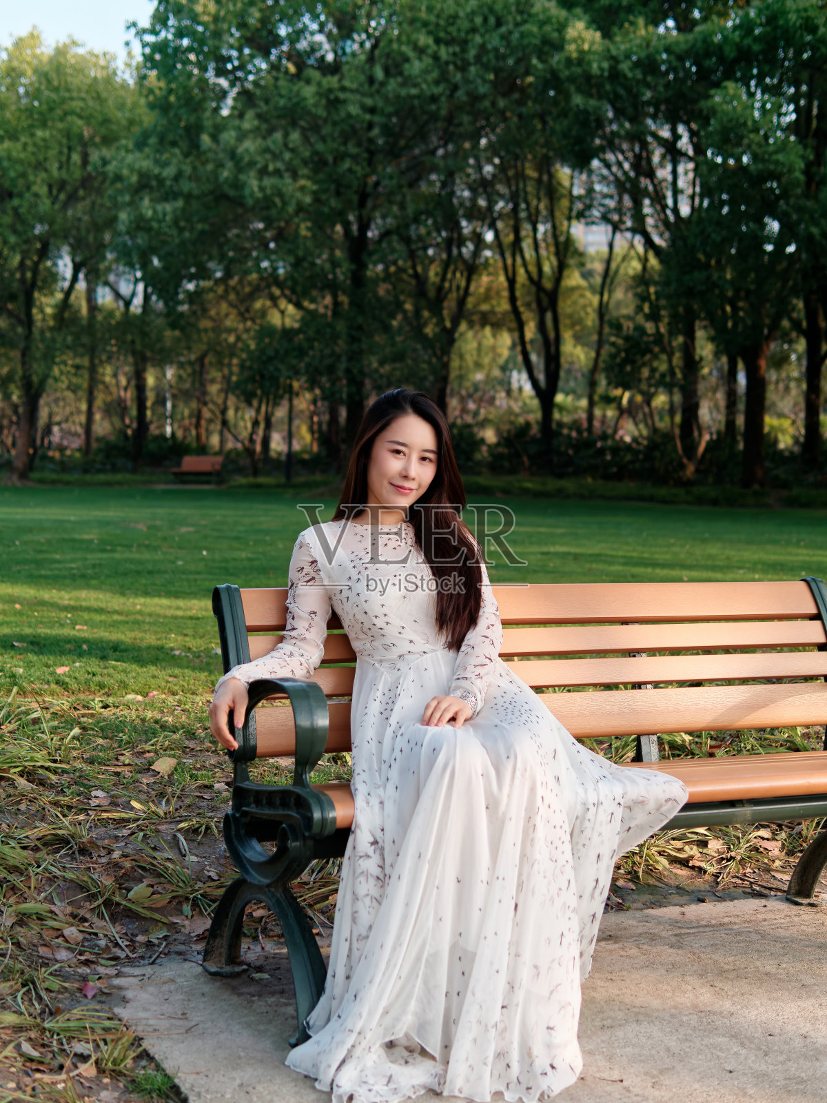 在阳光明媚的日子里，美丽的年轻中国女子微笑着看着森林公园背景的相机。照片摄影图片