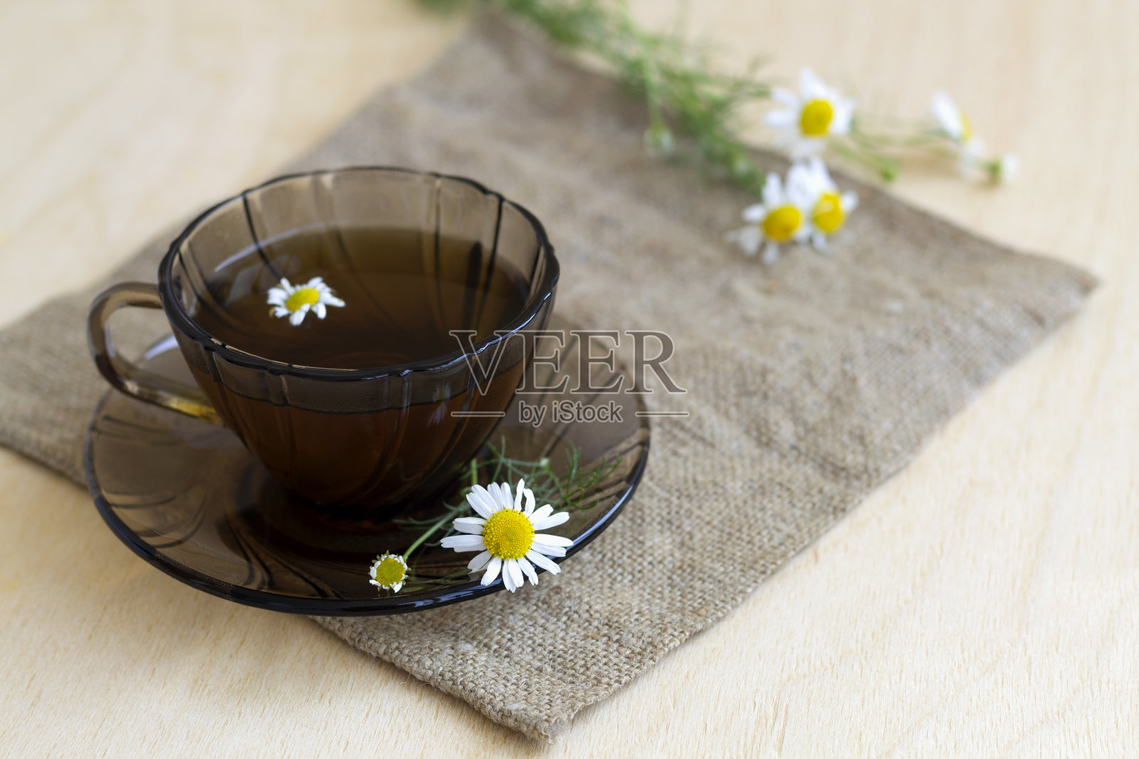 深色玻璃杯里放着一杯凉茶和甘菊茶，放在一张有复印空间的轻木桌上。杯茶，花束鲜花和绿色的叶子在黄色的背景。健康的生活方式照片摄影图片
