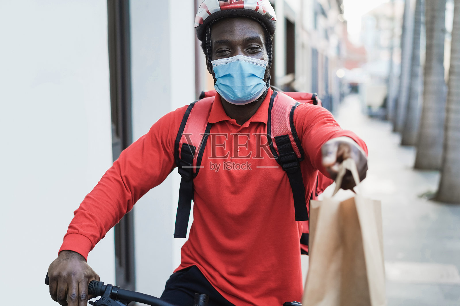 非洲骑手骑着电动车送餐，同时戴着防护面具-专注于脸部照片摄影图片