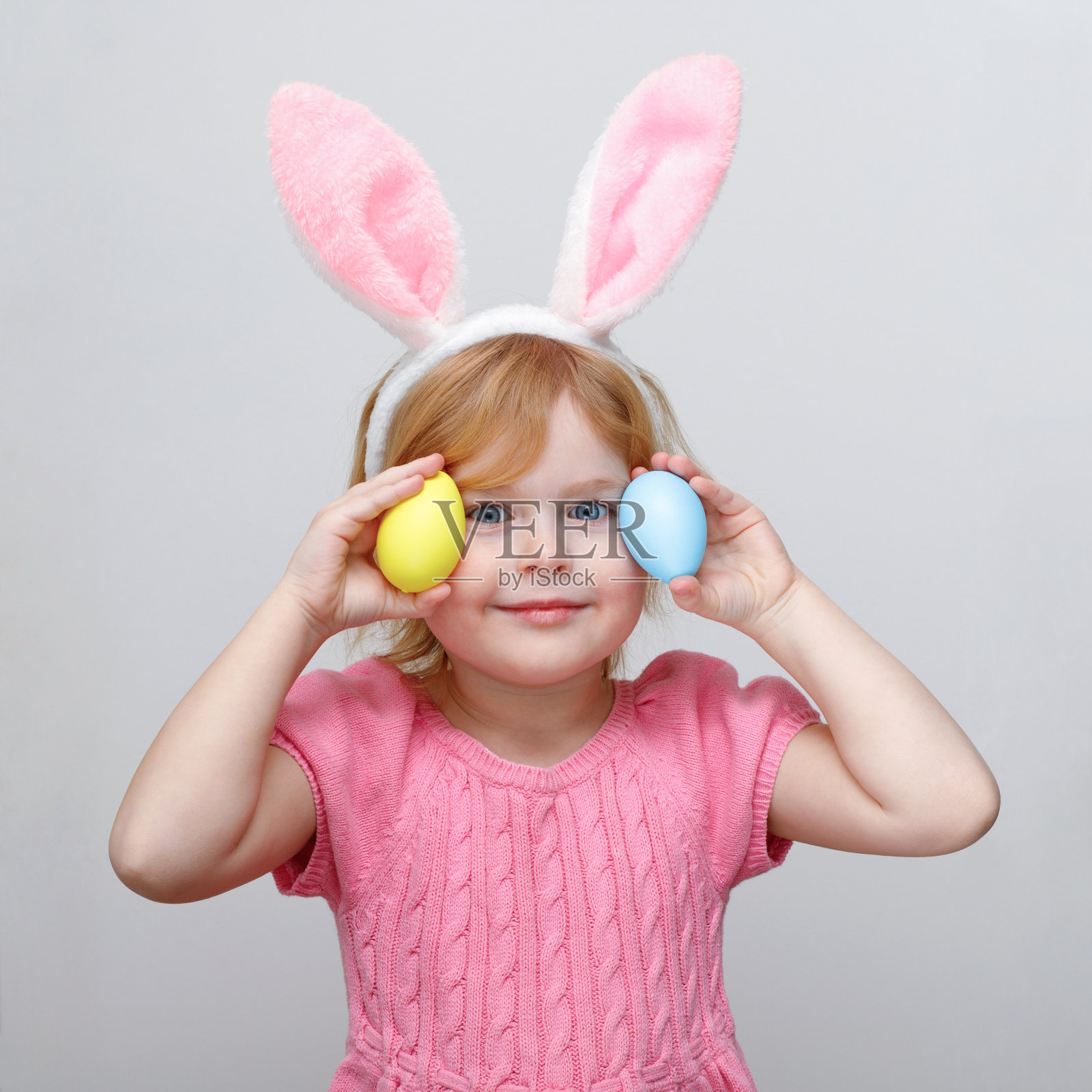 美丽微笑的小女孩戴着复活节兔子耳朵，拿着复活节彩蛋。照片摄影图片