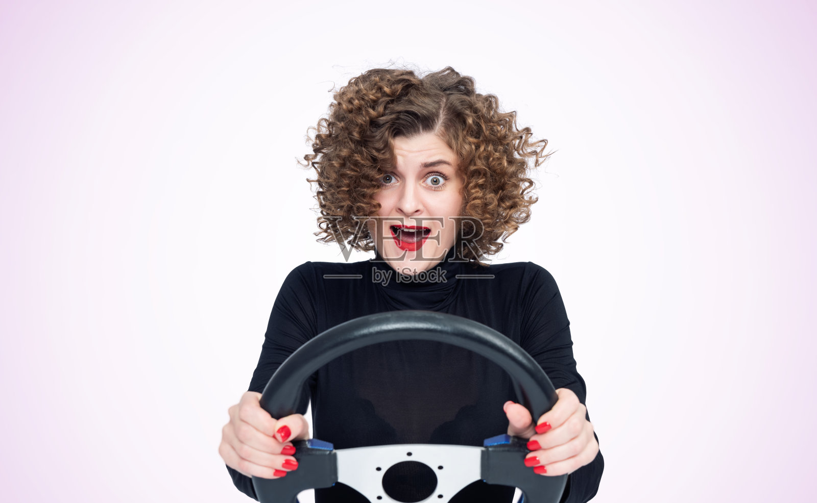 一个年轻的情绪紧张的女人，穿着黑色高领毛衣，开着一辆车，正面，浅粉色背景照片摄影图片