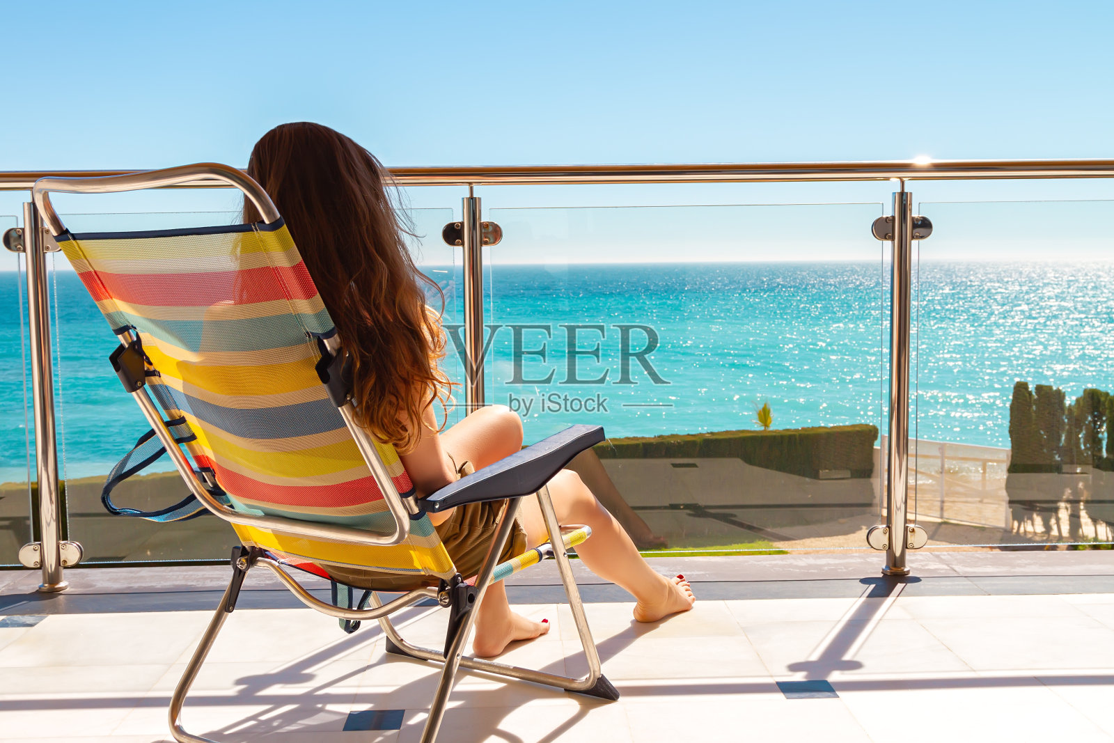 长头发的女孩坐在躺椅上，在阳台上晒日光浴，欣赏海景。照片摄影图片