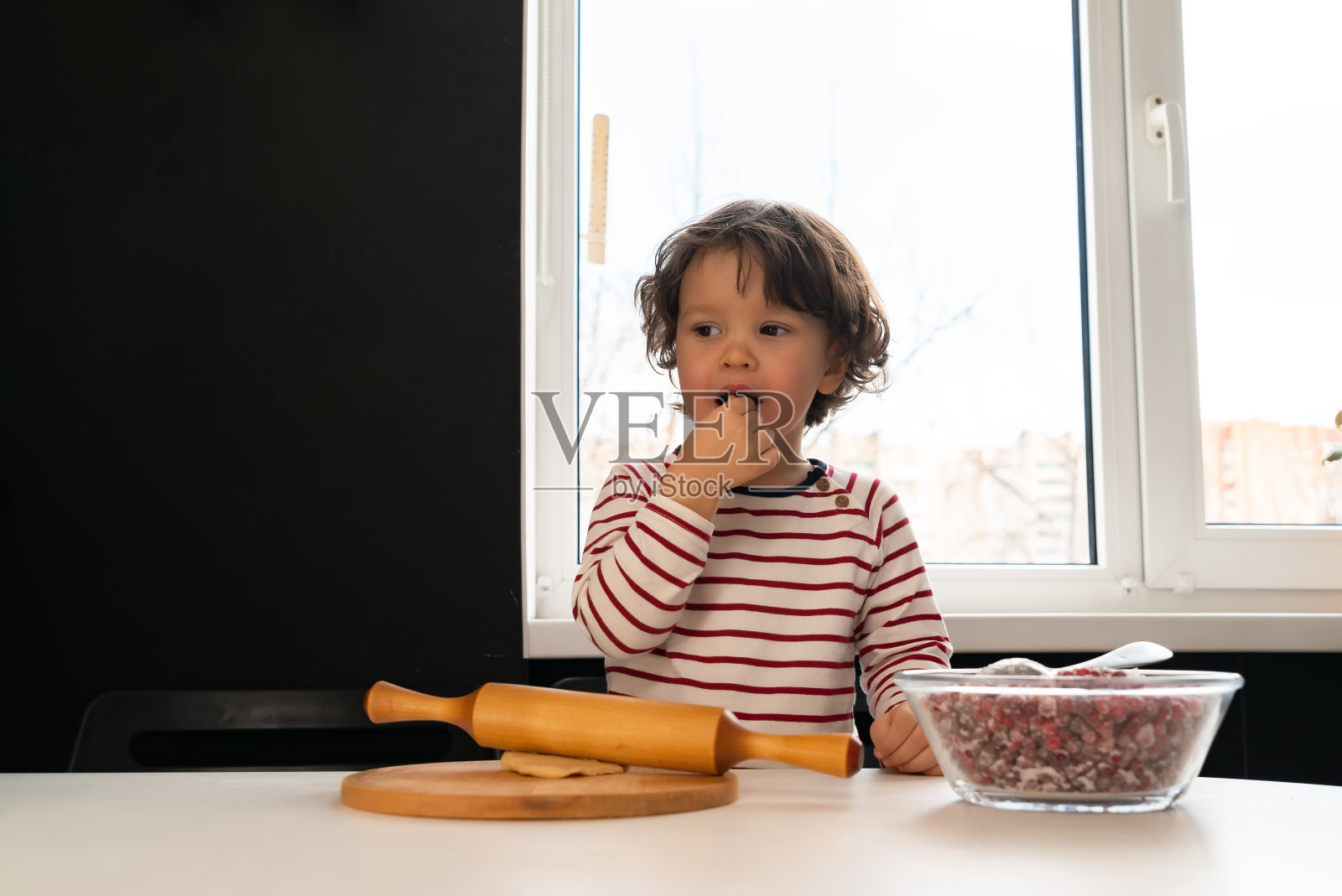小男孩在室内厨房用浆果做馅饼。照片摄影图片