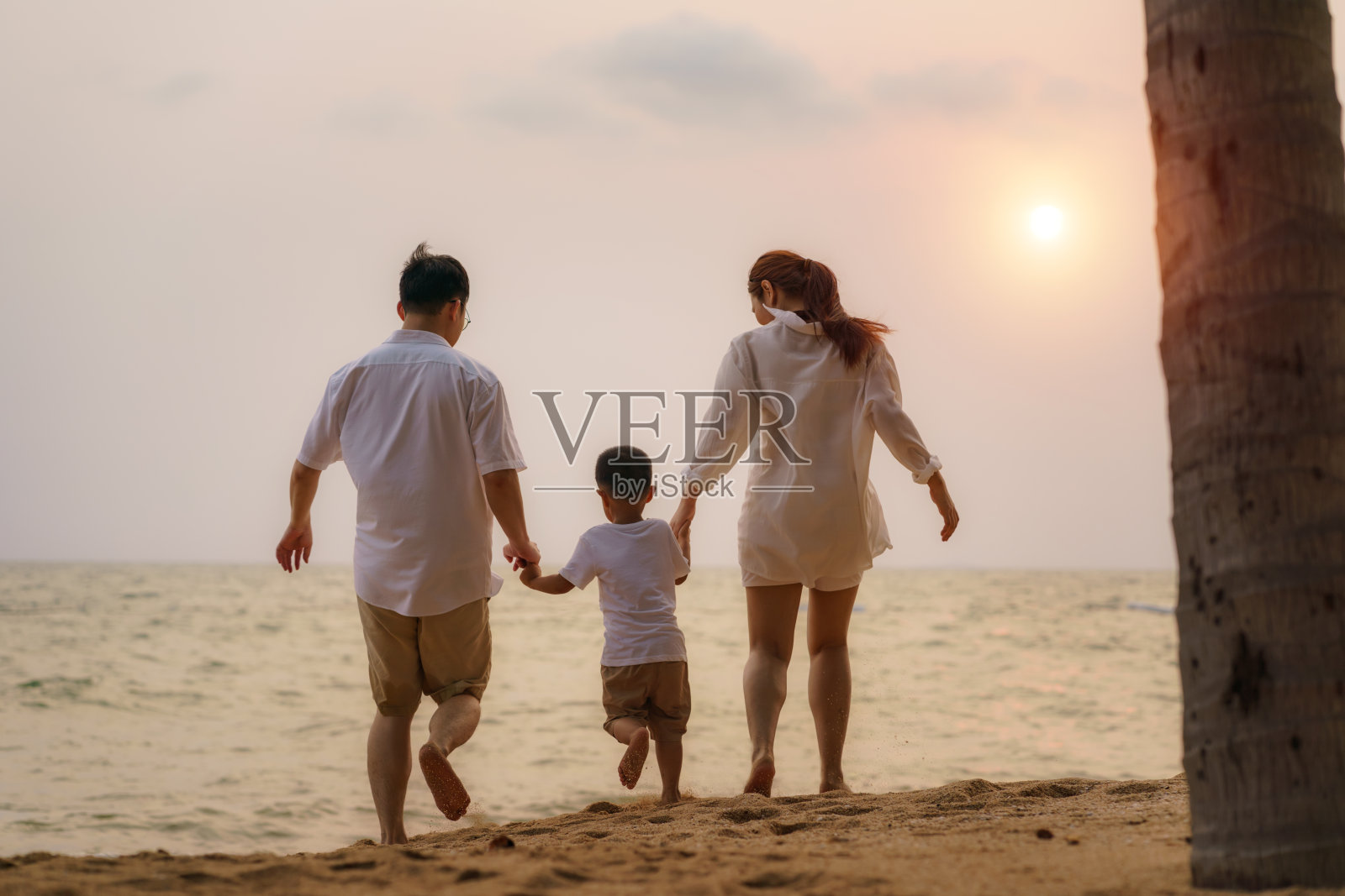 亚洲家庭与父亲，母亲和儿子在泰国度假的夏天沿着椰子树的海滨海滩散步。照片摄影图片