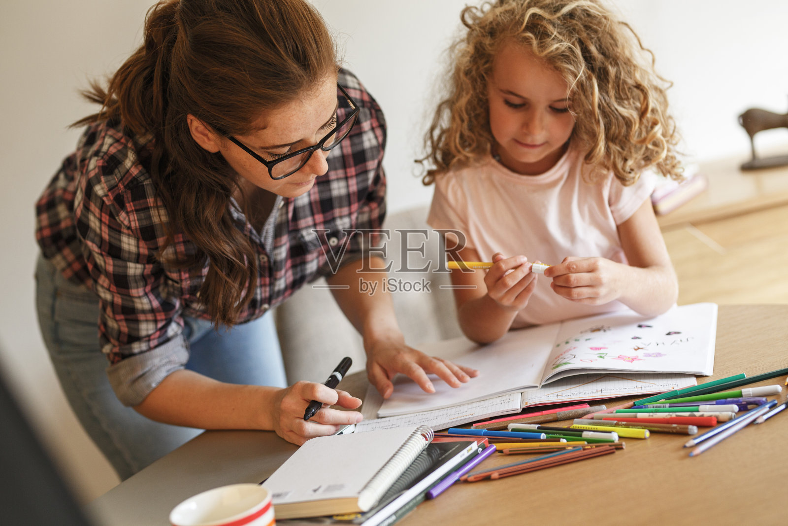 妈妈帮助她的女儿用彩色铅笔画画。照片摄影图片