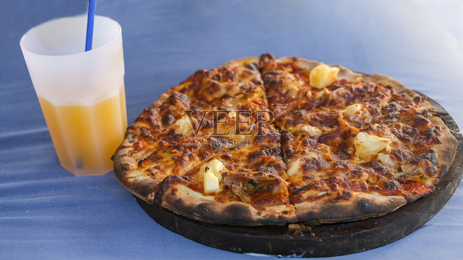 经典的圆形披萨放在木盘上，配上橙汁。蓝色背景。有选择性的重点。照片摄影图片