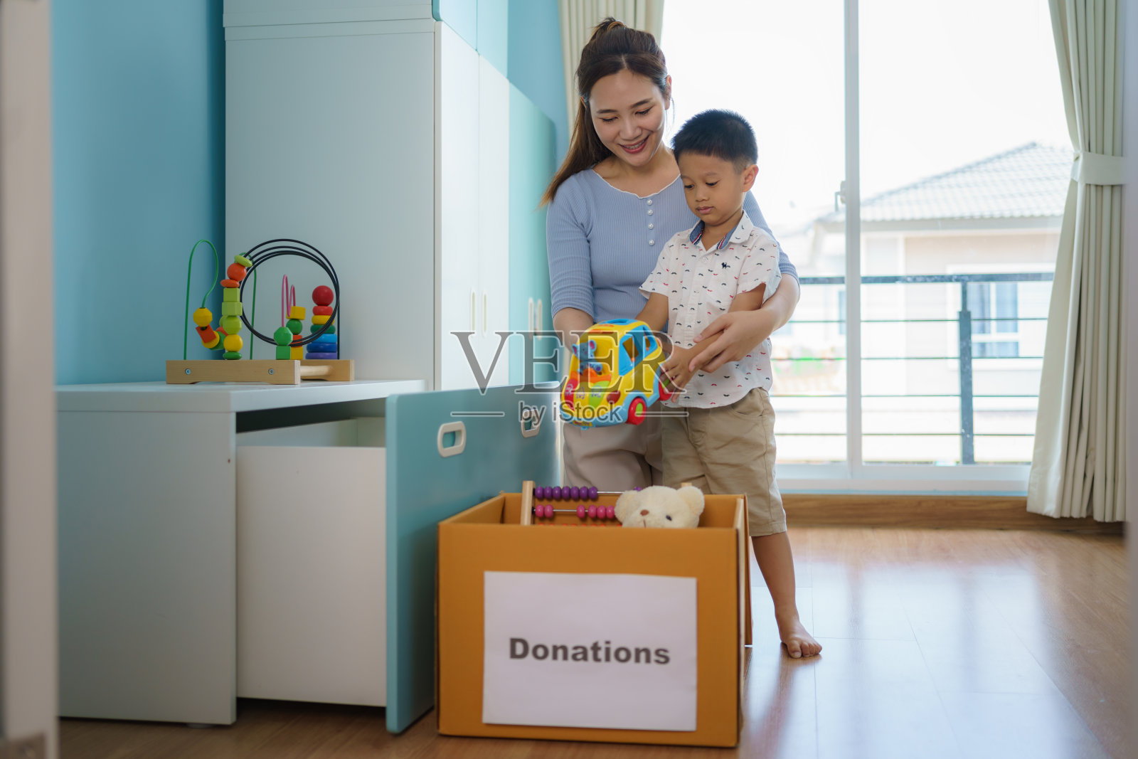 亚洲母亲和儿子正在为他们的孩子挑选不能玩的玩具，并把捐款箱送到捐赠中心。照片摄影图片