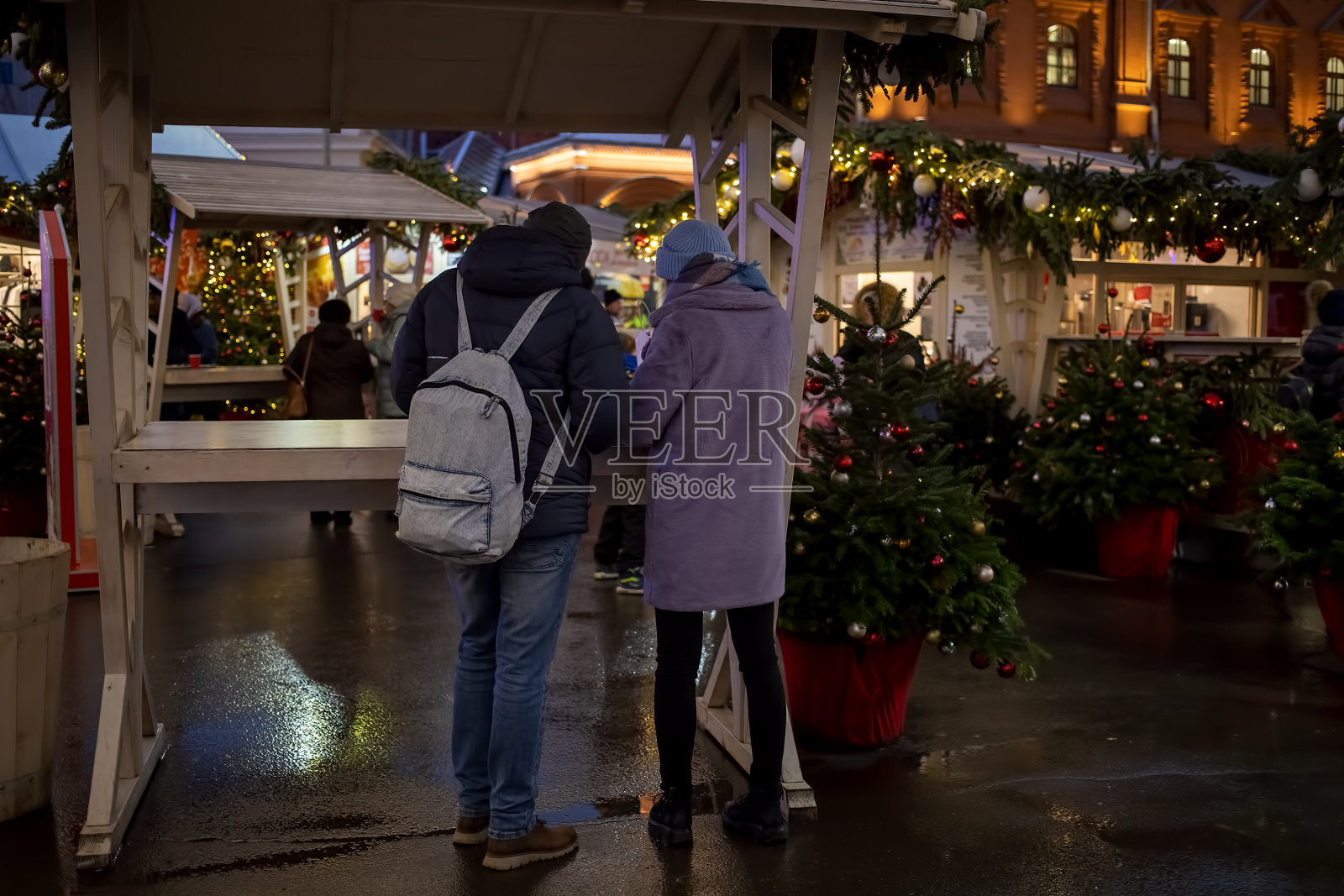 一对年轻夫妇和一对年轻夫妇站在餐桌上的美食广场在新年的市场和街道fair。后视图。在商场的背景和新年的装饰模糊照片摄影图片