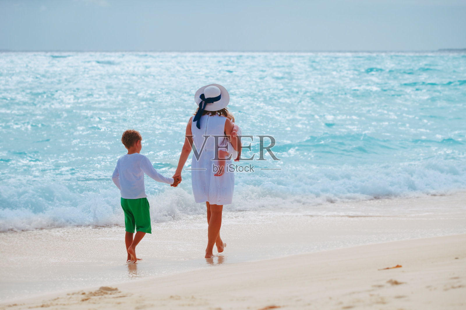 日落时分，母亲带着儿子和女儿在海滩上散步照片摄影图片