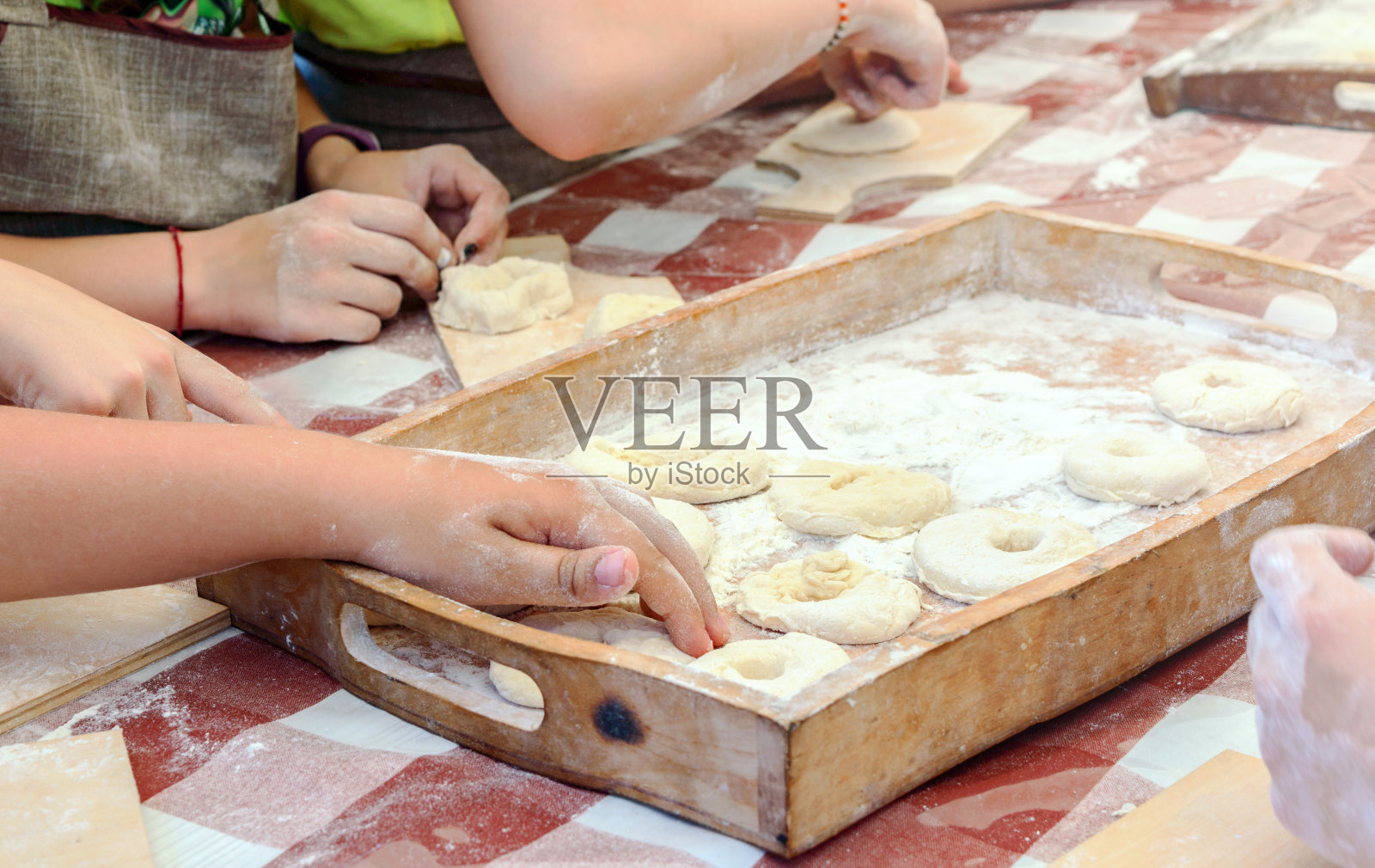 孩子们用生面团做甜甜圈，放在木制托盘上。烘焙大师班。照片摄影图片