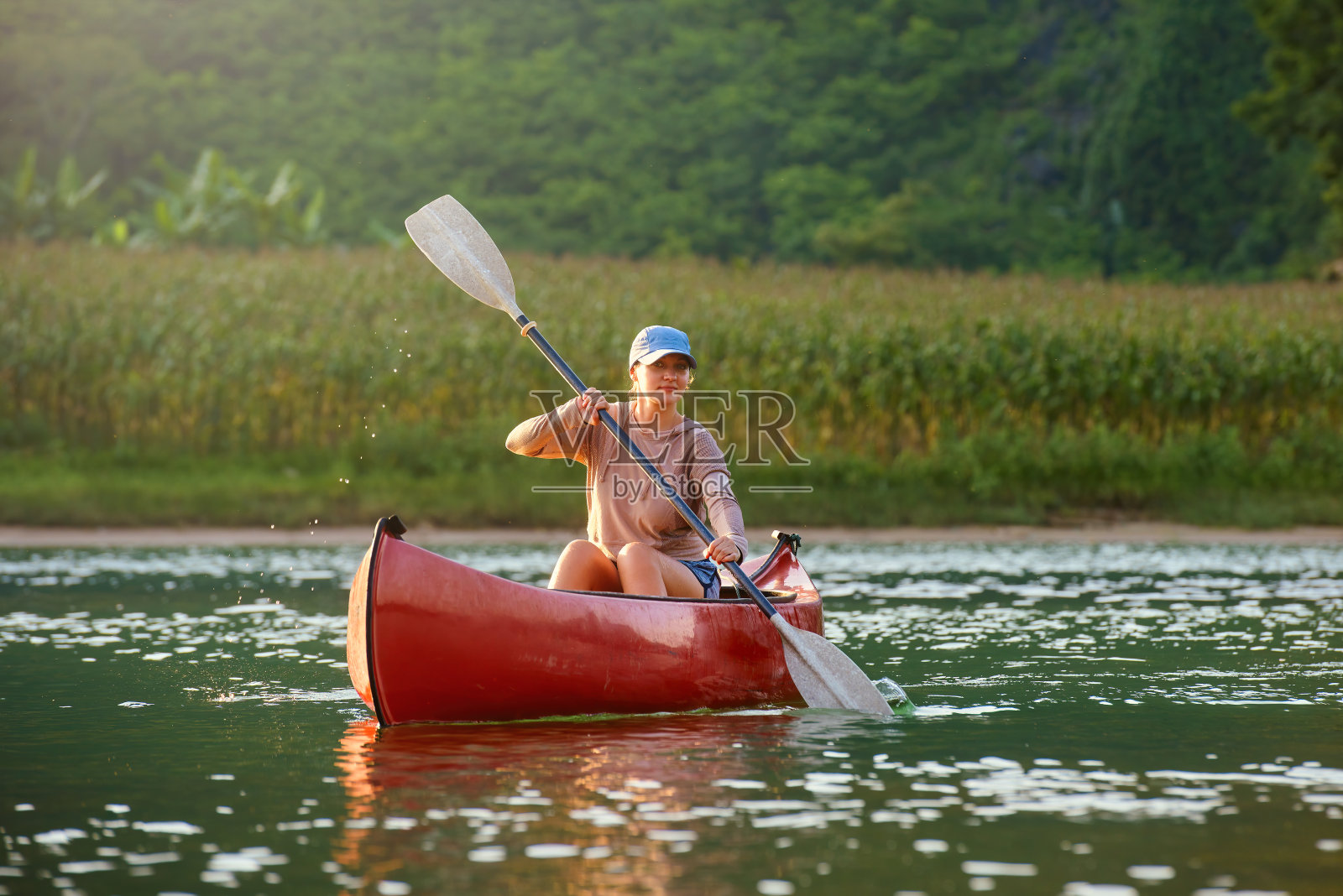 女人微笑着在乡村的河上泛舟皮划艇。照片摄影图片